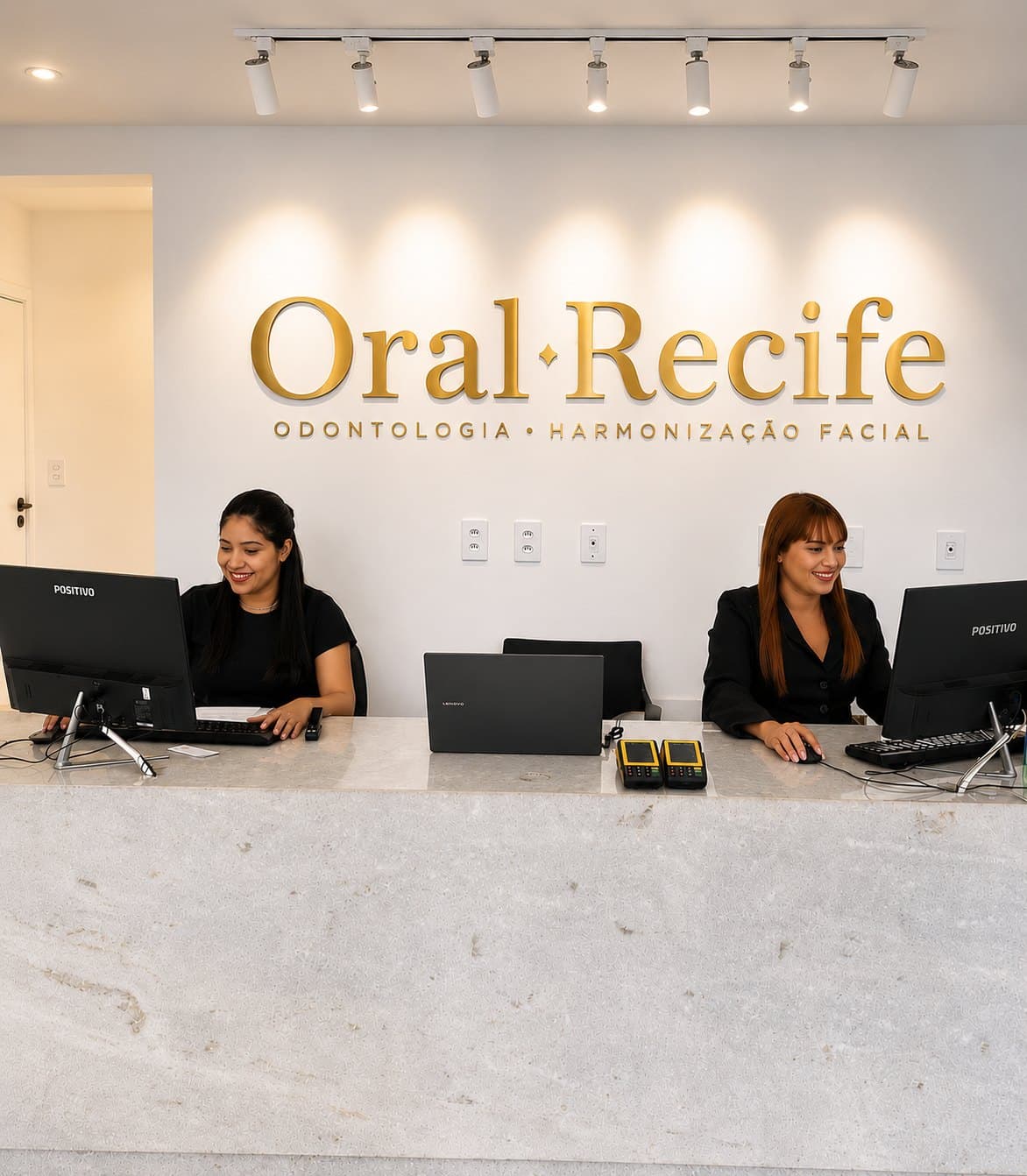 Recepção da Oral Recife com a equipe sorrindo atrás do balcão de mármore